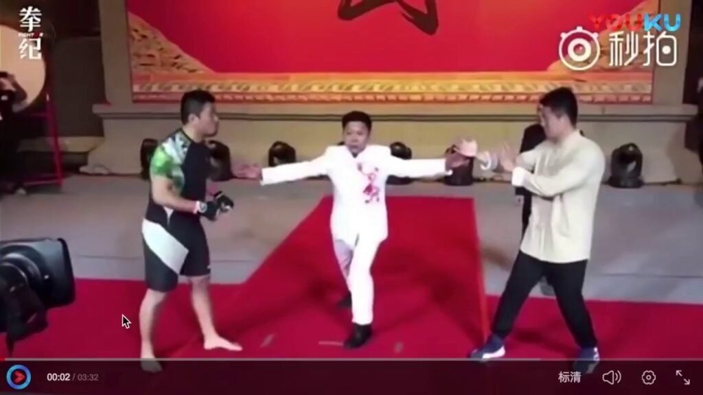 Why Isn’t Kung Fu as Popular as It Once Was? - man in a white suit stands between two fighters on a red carpet, extending his arms as if to demonstrate or mediate during a martial arts event.
